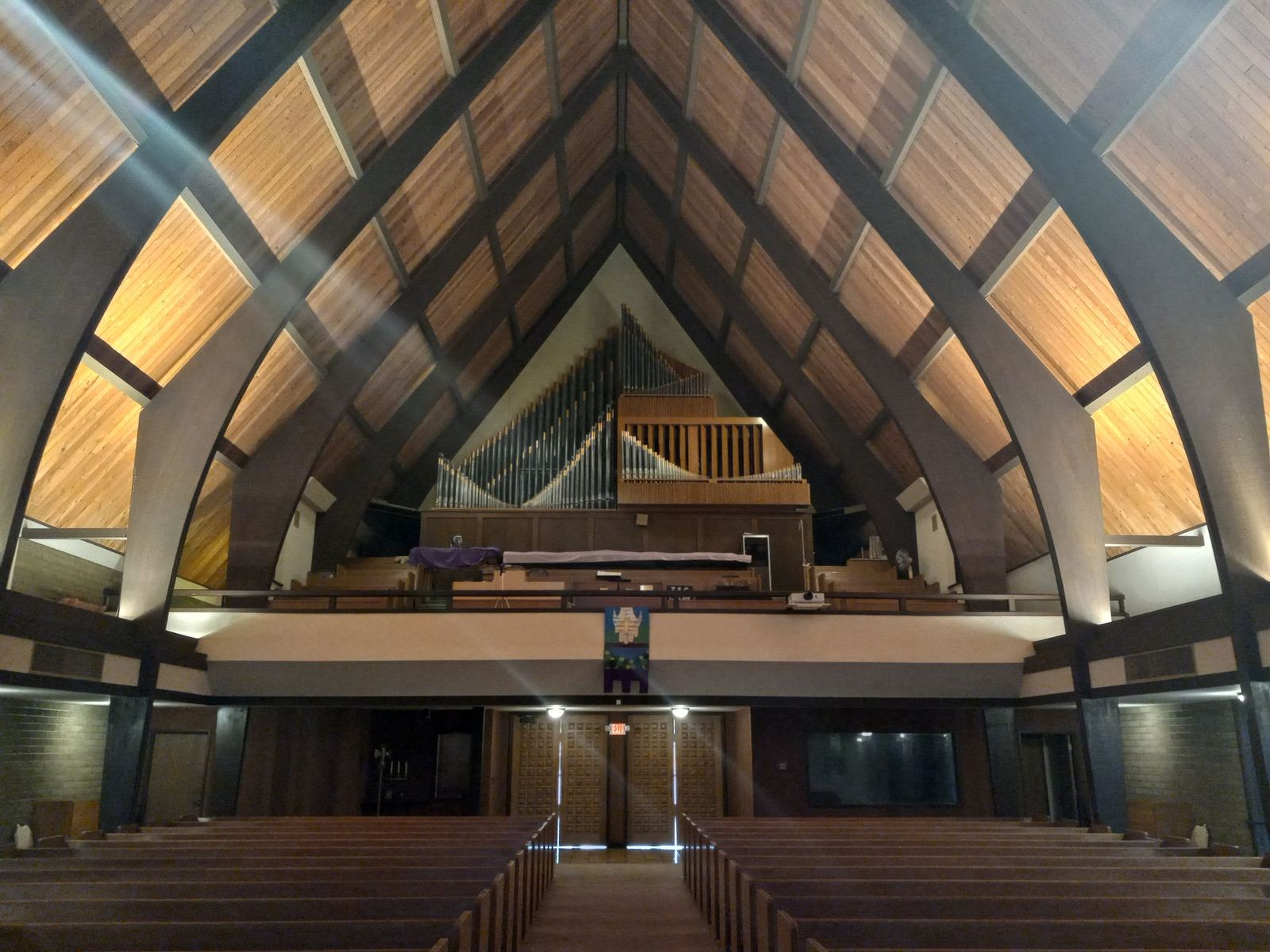 The nave seen from the front, looking back toward the pipe organ in the balcony, with light falling through the roof beams
