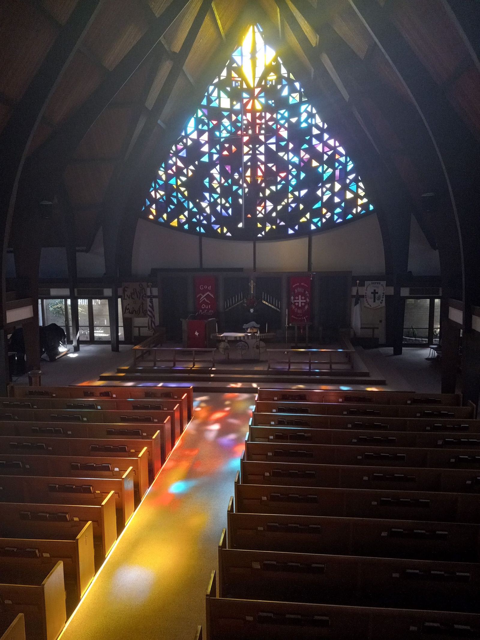 The chancel viewed from the balcony, with red paraments on the altar and pulpit and colored light scattered across the center aisle