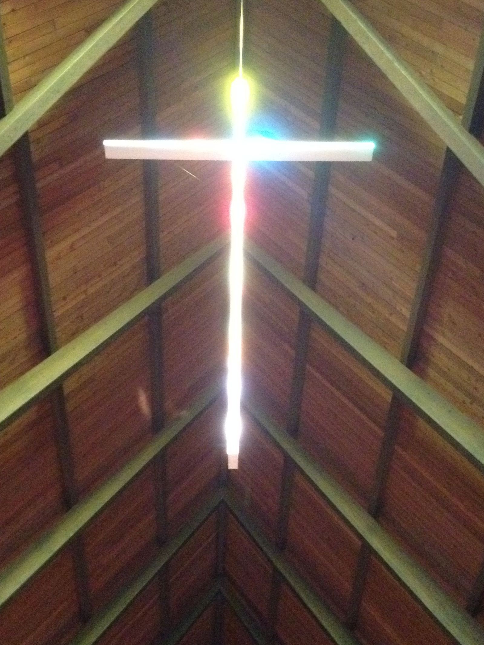 The hanging cross close up, catching the light, against the wooden boards of the sanctuary ceiling